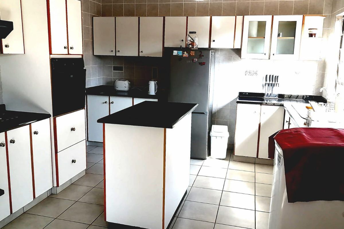 A functional kitchen featuring white cabinetry with contrasting trim, a central island, built-in oven, extractor fan, and tiled finishes throughout.