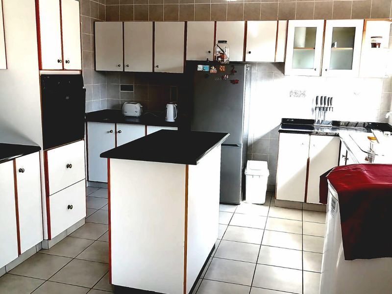 A functional kitchen featuring white cabinetry with contrasting trim, a central island, built-in oven, extractor fan, and tiled finishes throughout.