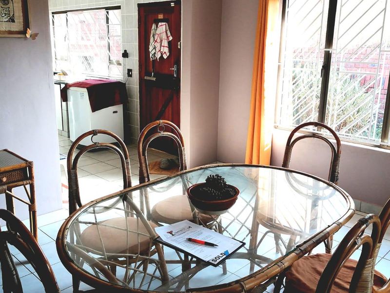 Open plan dining area featuring tiled flooring and security bars on windows, with an adjacent kitchen area visible in the background.