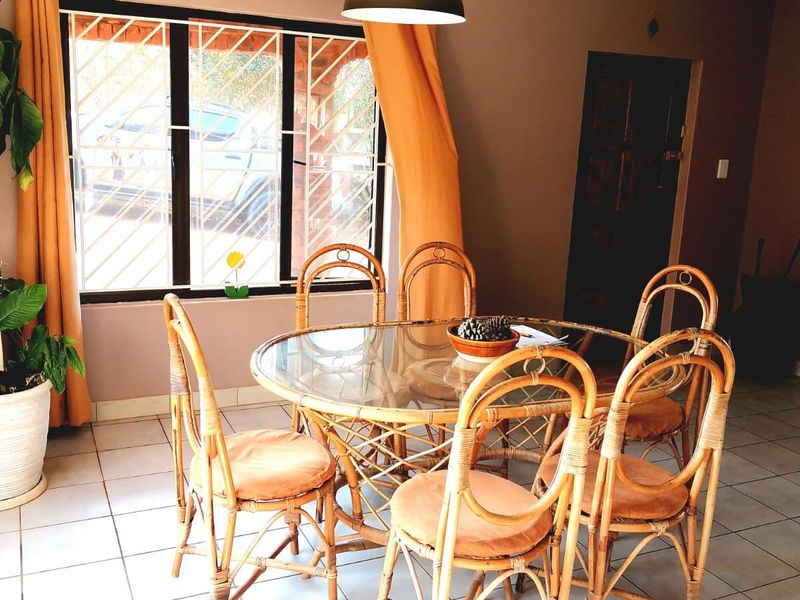 A dining area featuring tiled flooring, a large window with security bars, and a central pendant light fixture.