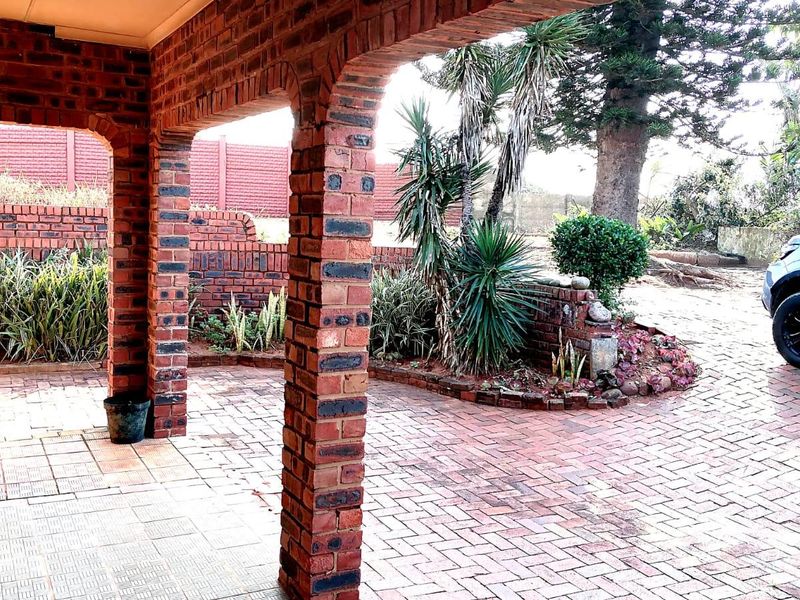 A covered patio area featuring exposed brick pillars and brick paving, overlooking a landscaped garden with a brick boundary wall.