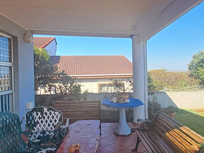 A covered outdoor patio area featuring tiled flooring and direct access to the garden through sliding glass doors.
