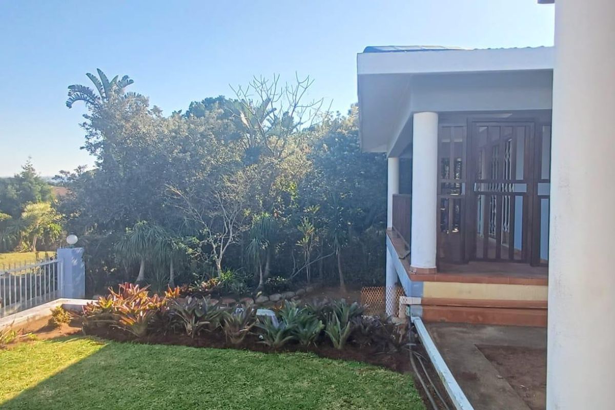 Rear view of the property featuring a covered patio area, concrete columns, and a well-maintained garden with established landscaping.