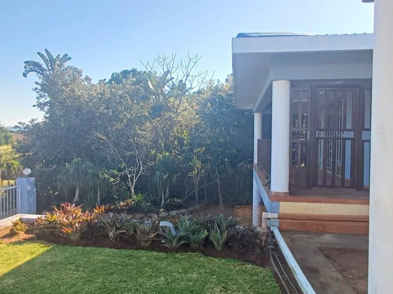 Rear view of the property featuring a covered patio area, concrete columns, and a well-maintained garden with established landscaping.