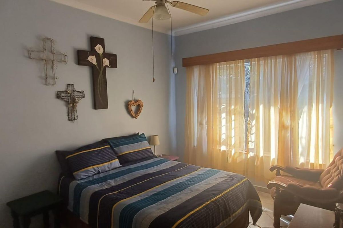 A bedroom featuring tiled flooring, a ceiling fan, and a large window with curtain rod, providing natural light.