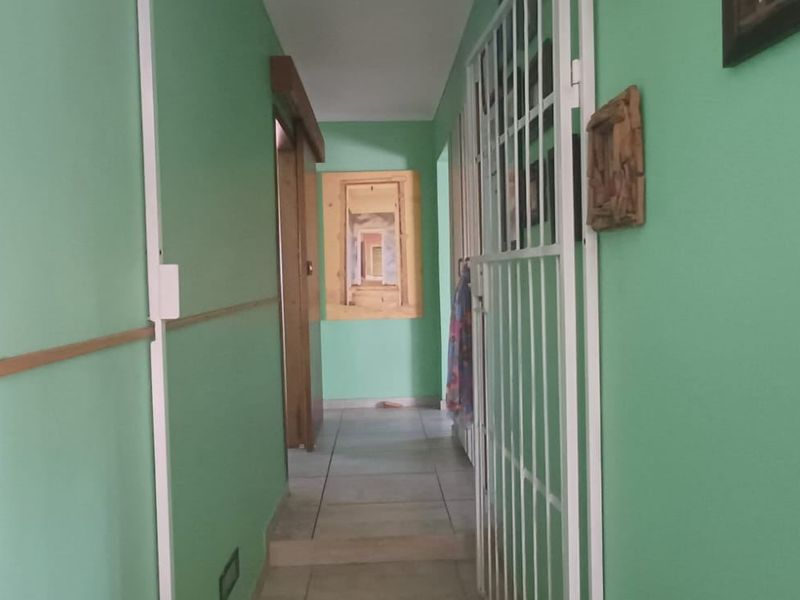 A narrow interior hallway featuring tiled flooring and a white security gate, finished with green wall paint.