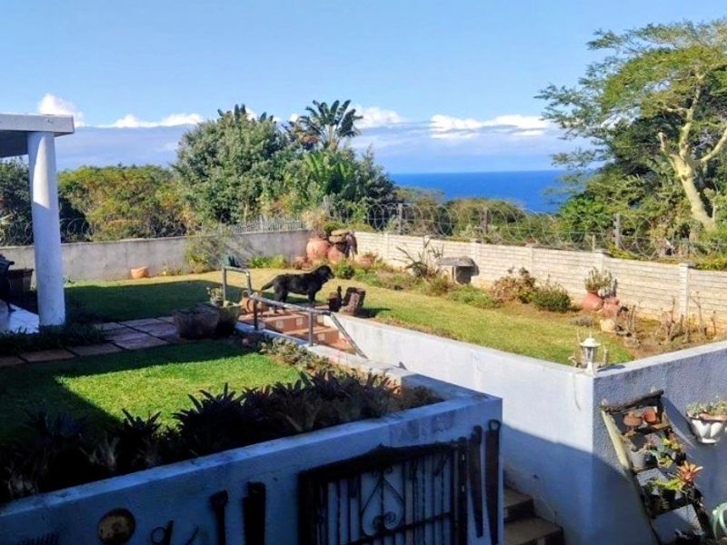 A rear garden area featuring a covered patio, concrete boundary walls with security fencing, and scenic ocean views.