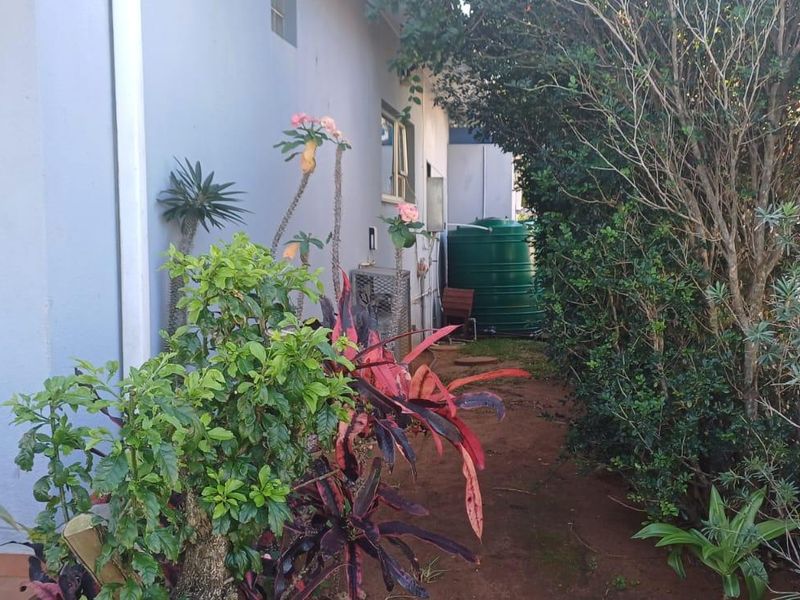 Side garden area featuring a green water storage tank, established landscaping, and exterior building infrastructure.
