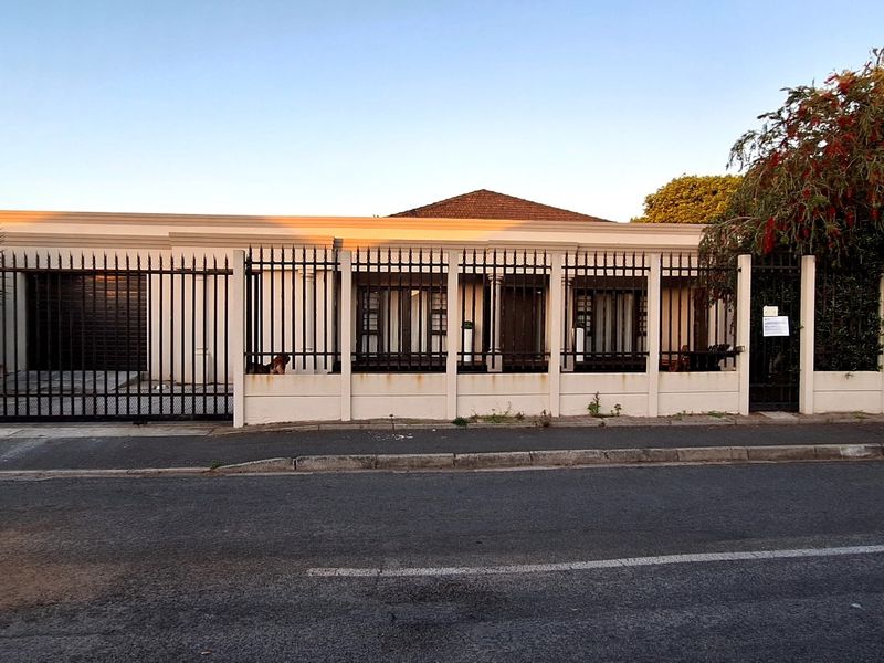 Front elevation of the property featuring a secure boundary wall with wrought iron fencing and a garage entrance.