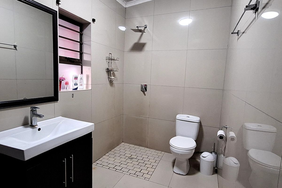 Modern bathroom featuring a vanity with basin, wall-mounted mirror, walk-in shower area, and toilet with neutral floor-to-ceiling tiling.