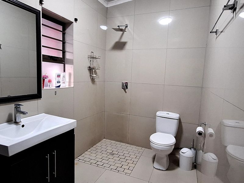 Modern bathroom featuring a vanity with basin, wall-mounted mirror, walk-in shower area, and toilet with neutral floor-to-ceiling tiling.