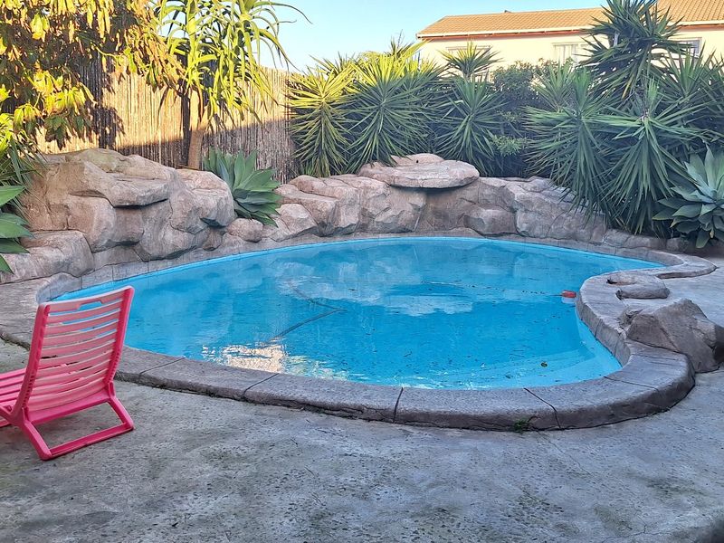 Outdoor pool area featuring a rock-scaped swimming pool surrounded by concrete paving and established garden greenery.