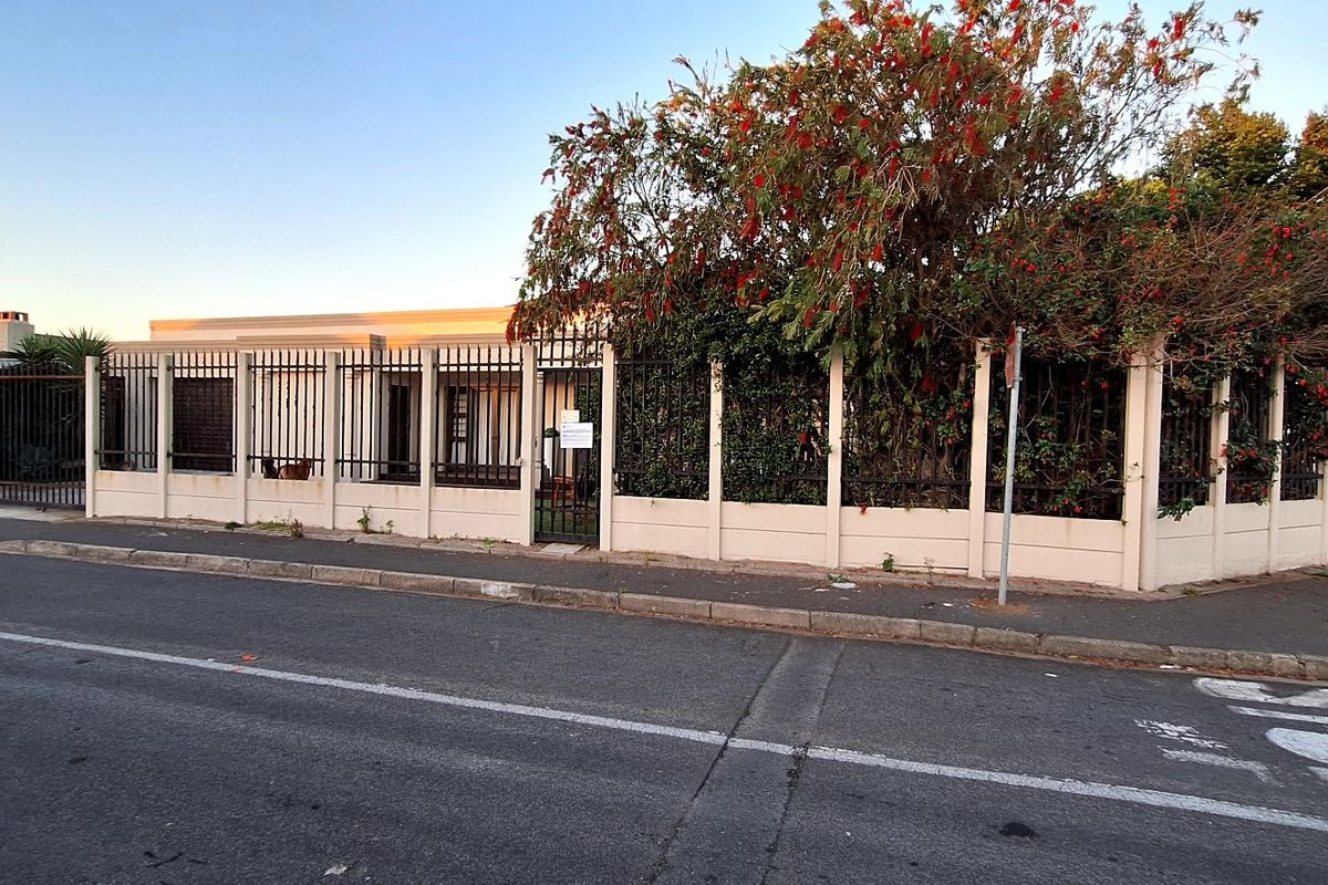 Front exterior view of the property featuring a secure perimeter fence, gated entrance, and established garden foliage along the street boundary.