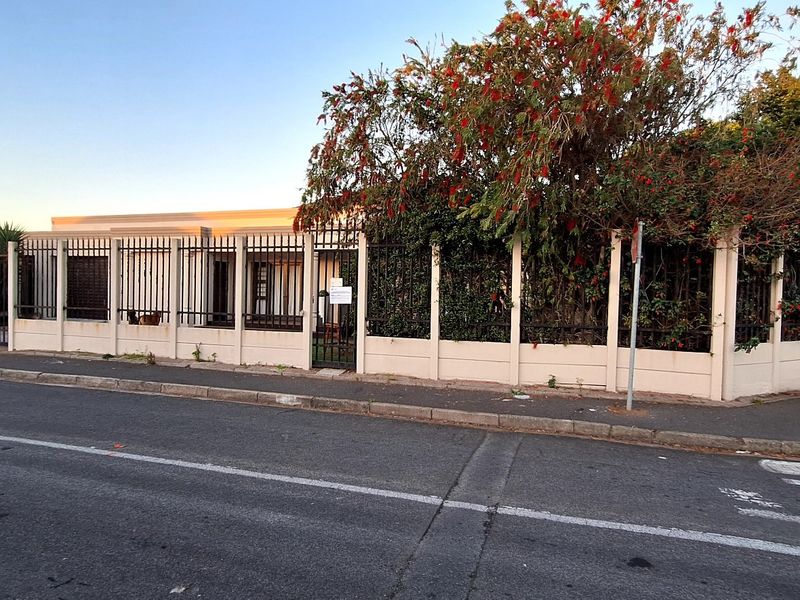 Front exterior view of the property featuring a secure perimeter fence, gated entrance, and established garden foliage along the street boundary.