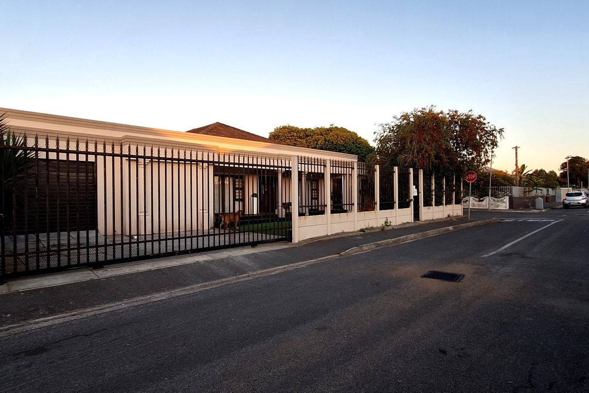 Front exterior view of the property featuring a secure wrought iron fence, sliding gate, and concrete boundary wall along the street.