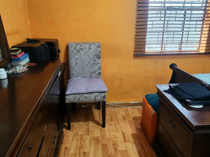 A bedroom featuring laminate flooring and venetian blinds, currently showing signs of wear on the wall surfaces.