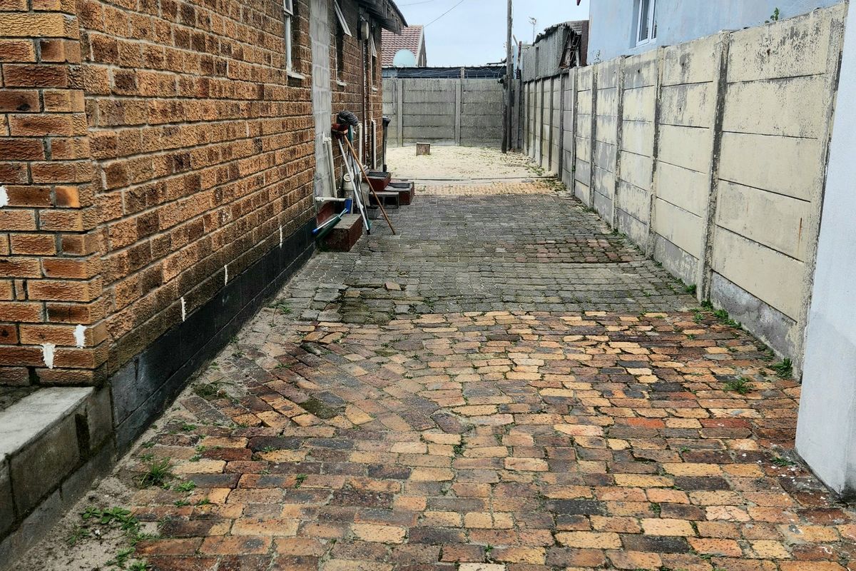 A narrow side passage featuring brick paving and precast concrete boundary walls, showing signs of wear and maintenance requirements.