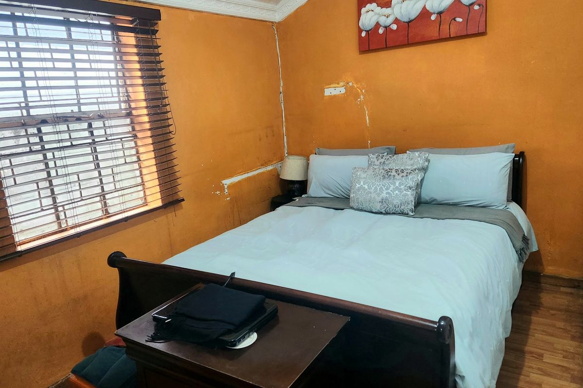 A bedroom featuring laminate flooring and venetian blinds, currently showing significant signs of wear including ceiling water damage and peeling wall paint.
