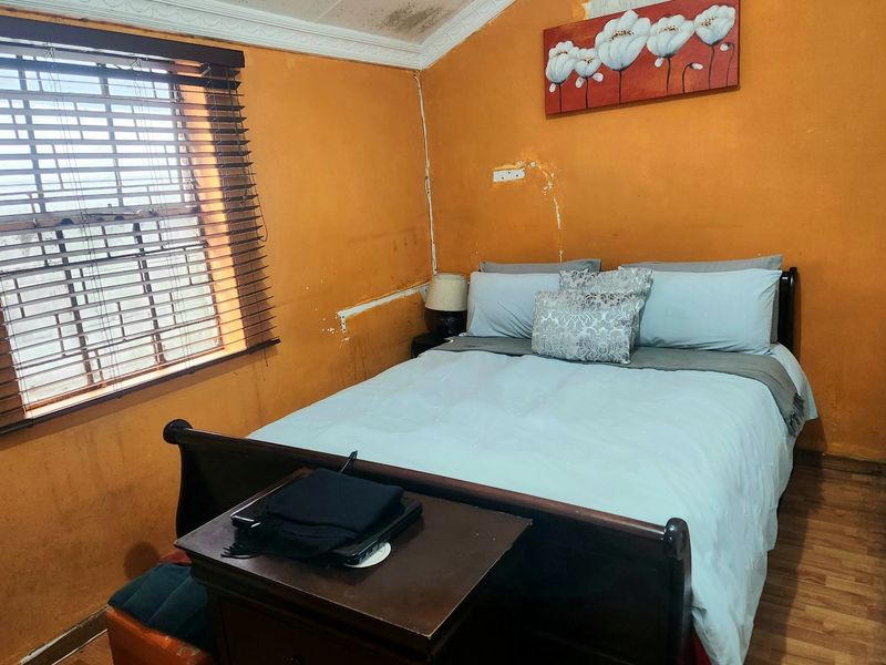 A bedroom featuring laminate flooring and venetian blinds, currently showing significant signs of wear including ceiling water damage and peeling wall paint.