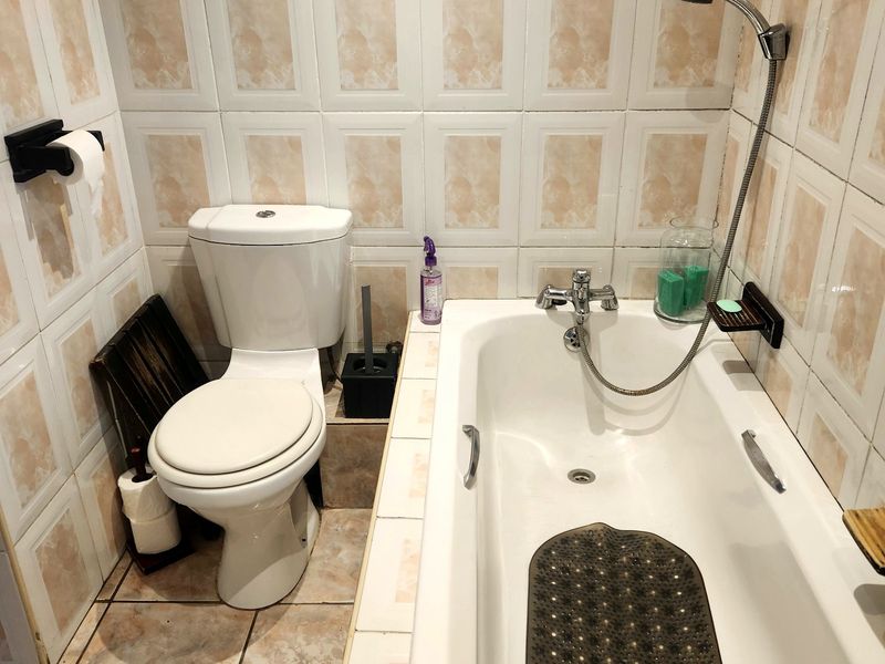A compact bathroom featuring a standard bathtub with a handheld shower attachment and a white toilet, finished with dated ceramic wall and floor tiles.