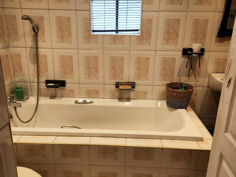 A compact bathroom featuring a built-in bathtub with a handheld shower attachment, tiled walls, and tiled flooring.