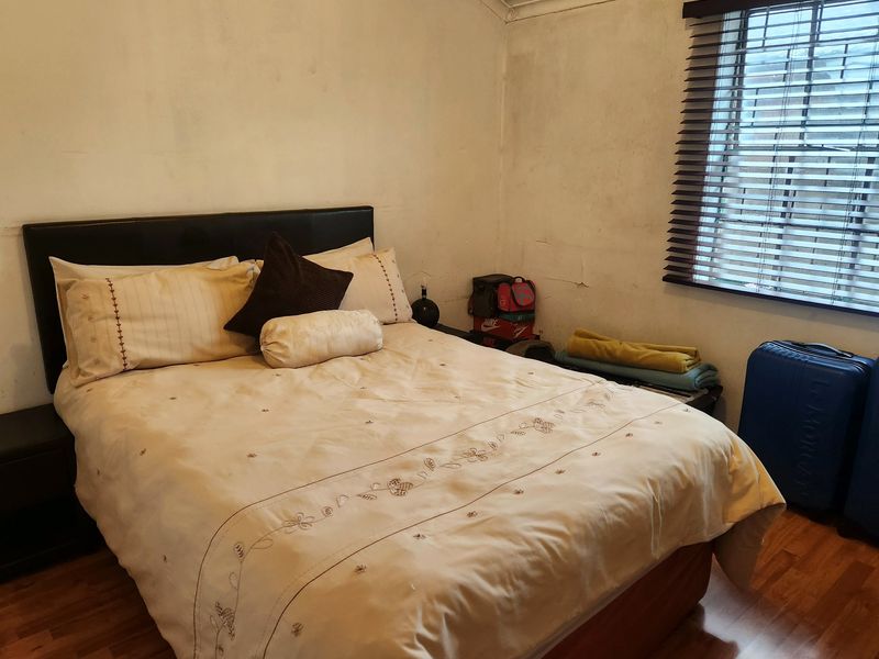 A bedroom featuring laminate flooring and venetian blinds, currently showing significant signs of wear including cracked and stained wall finishes.