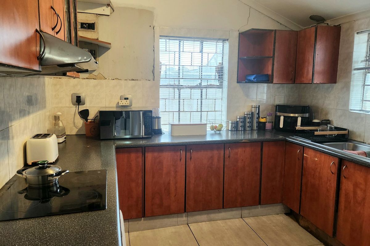A functional kitchen featuring wood-look cabinetry, dark laminate countertops, and an electric hob, currently showing signs of wear and requiring cosmetic updates.