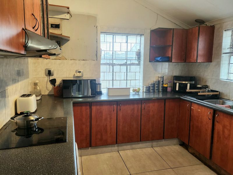 A functional kitchen featuring wood-look cabinetry, dark laminate countertops, and an electric hob, currently showing signs of wear and requiring cosmetic updates.
