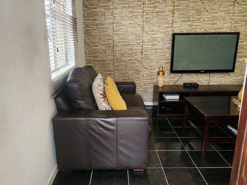 A living room featuring dark tiled flooring, a stone veneer accent wall, and ceiling tiles, offering a base for potential cosmetic updates.