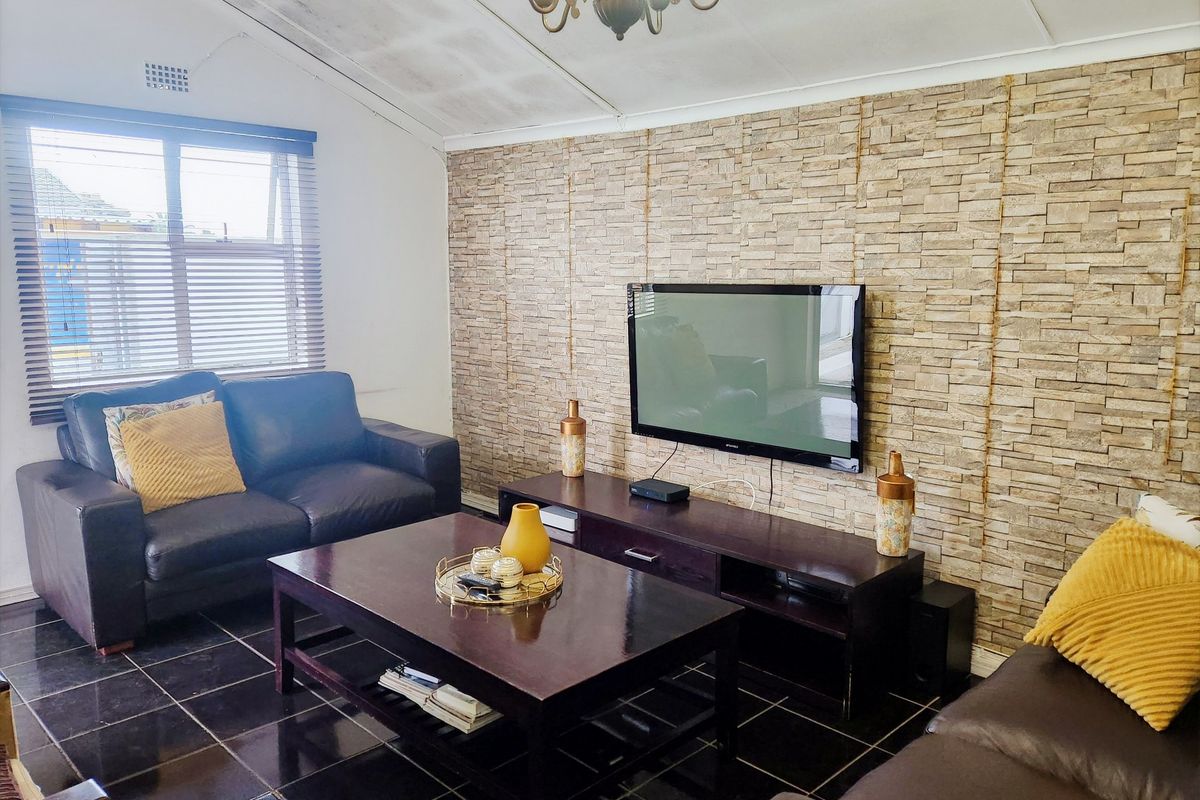 A living room featuring a stone veneer accent wall, dark tiled flooring, and a vaulted ceiling with visible water damage.