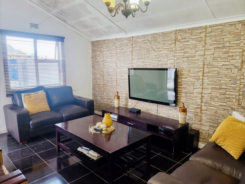 A living room featuring a stone veneer accent wall, dark tiled flooring, and a vaulted ceiling with visible water damage.