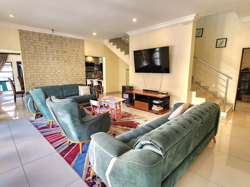 Spacious open-plan living area featuring a stone accent wall, tiled flooring, and a modern staircase with stainless steel railings.