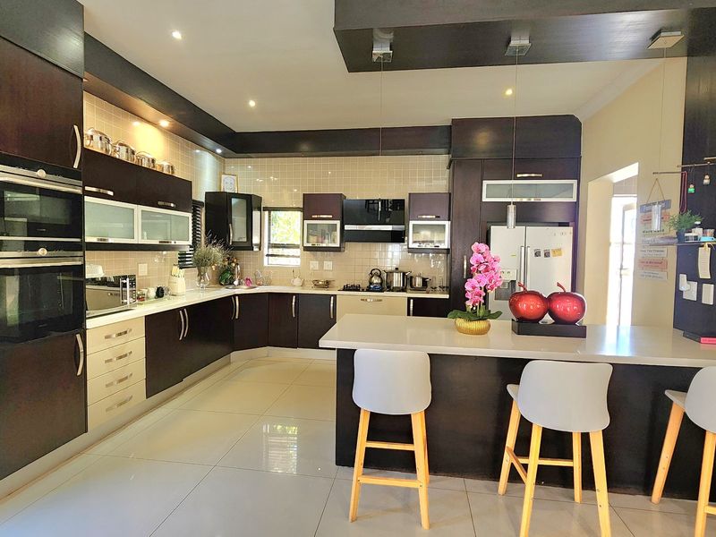 Modern kitchen featuring dark cabinetry, a central island with breakfast bar seating, built-in appliances, and tiled flooring throughout.