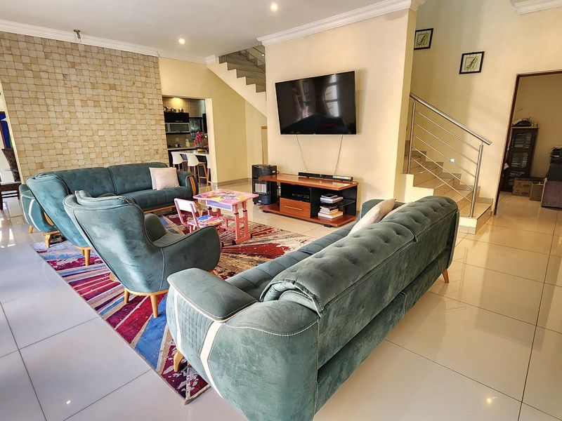 Spacious open-plan living area featuring a textured stone feature wall, tiled flooring, and a modern staircase with a stainless steel balustrade.
