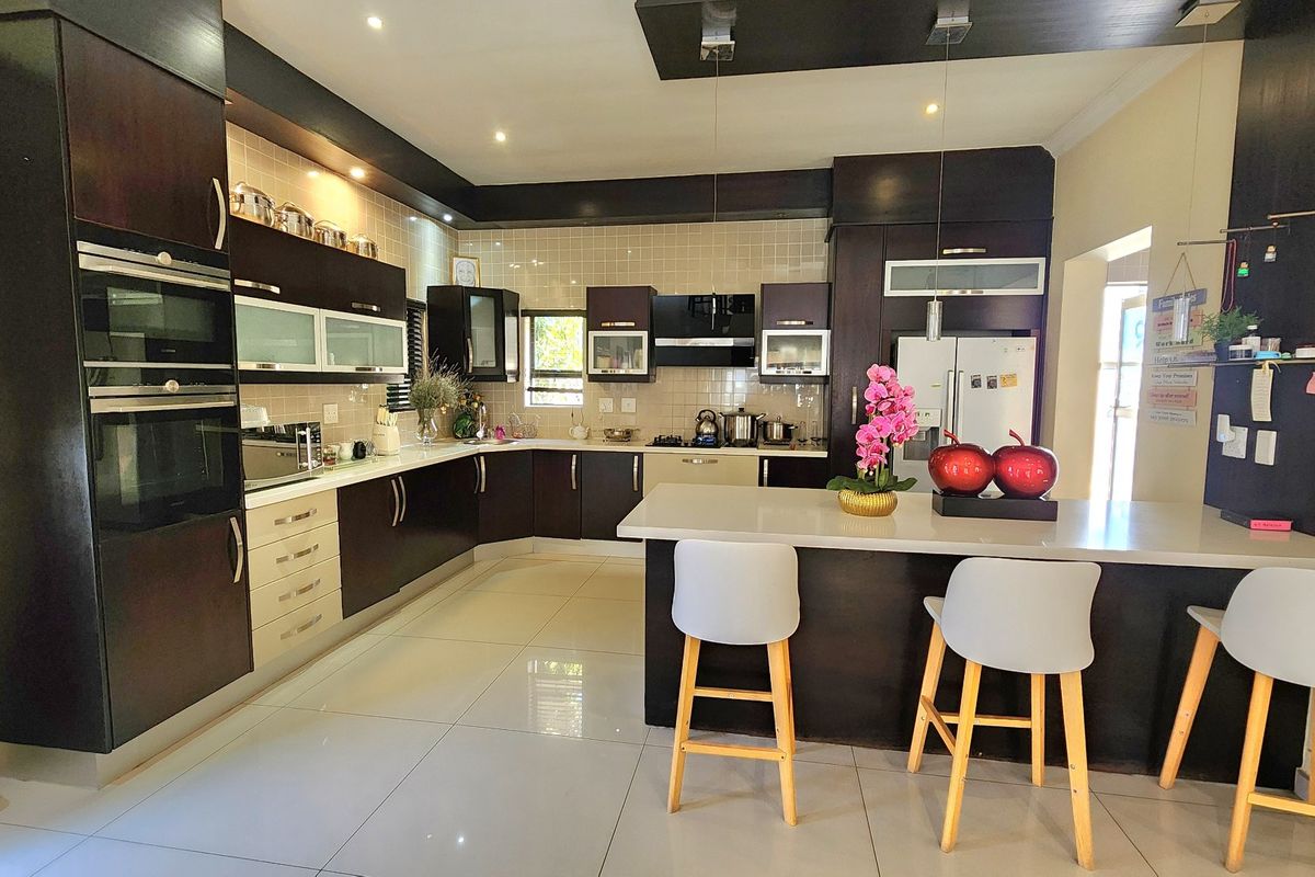 A modern kitchen featuring dark cabinetry, stone countertops, a central island with breakfast bar seating, and integrated built-in appliances.