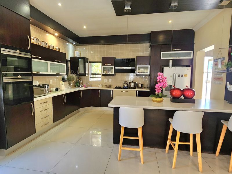 A modern kitchen featuring dark cabinetry, stone countertops, a central island with breakfast bar seating, and integrated built-in appliances.