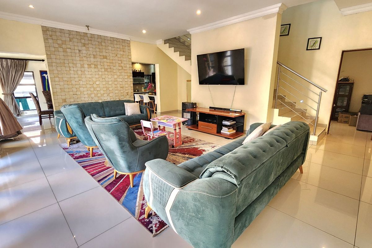 Spacious open-plan living area featuring a stone accent wall, tiled flooring, and a modern staircase with a stainless steel balustrade.