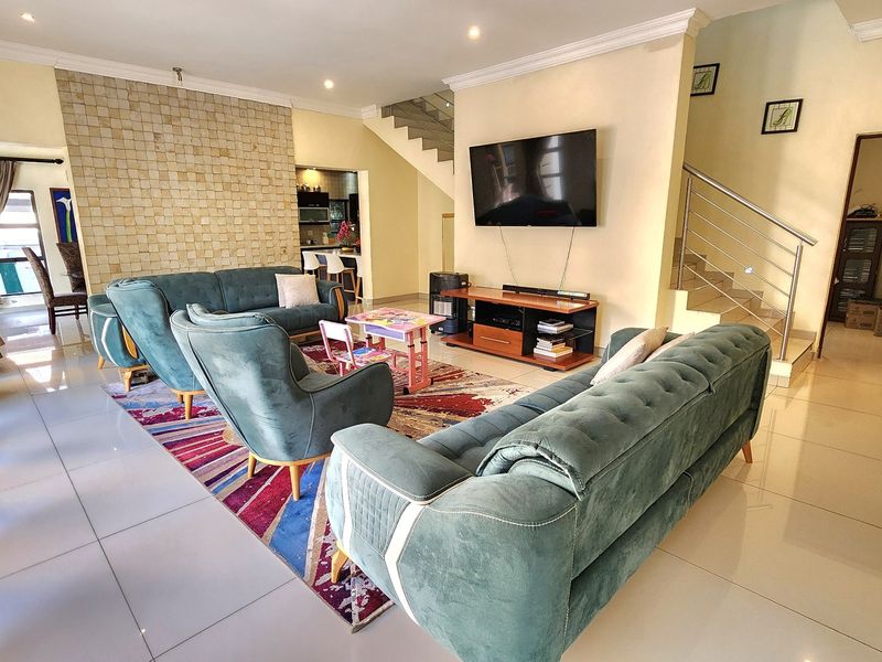 Spacious open-plan living area featuring a stone accent wall, tiled flooring, and a modern staircase with a stainless steel balustrade.