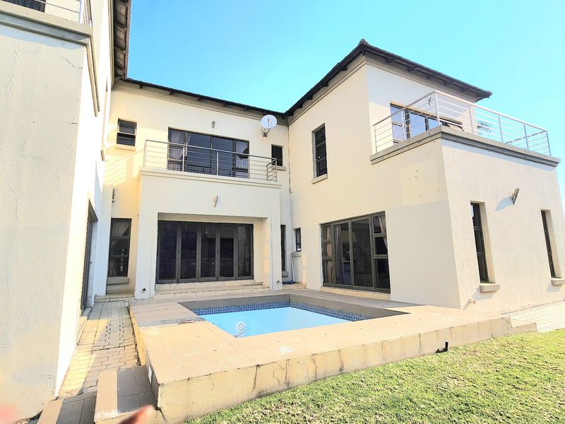 Rear view of the property featuring a swimming pool, paved patio area, and upper-level balconies with stainless steel railings.