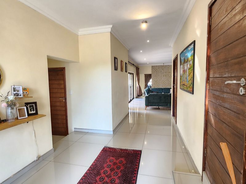 A bright and spacious hallway featuring polished tiled flooring, recessed downlighting, and classic wooden doors leading to adjacent rooms.
