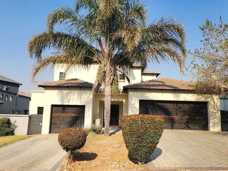 Front elevation of a double-story house featuring a paved driveway, double garage, and established palm tree landscaping.