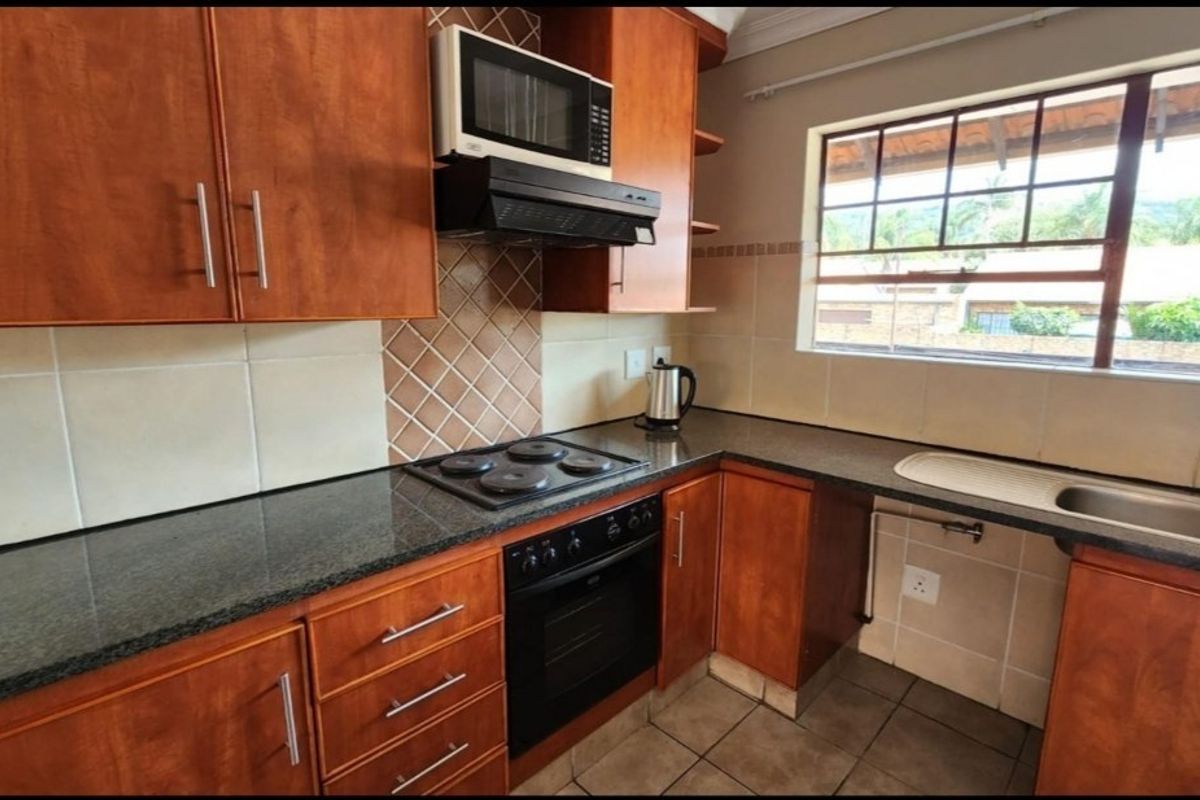 Functional kitchen featuring wood-finish cabinetry, granite countertops, built-in oven, electric hob, and a tiled splashback with natural light from the window.