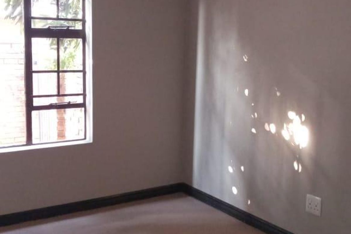 A clean, empty bedroom featuring neutral wall paint, carpeted flooring, and a window with a metal frame.