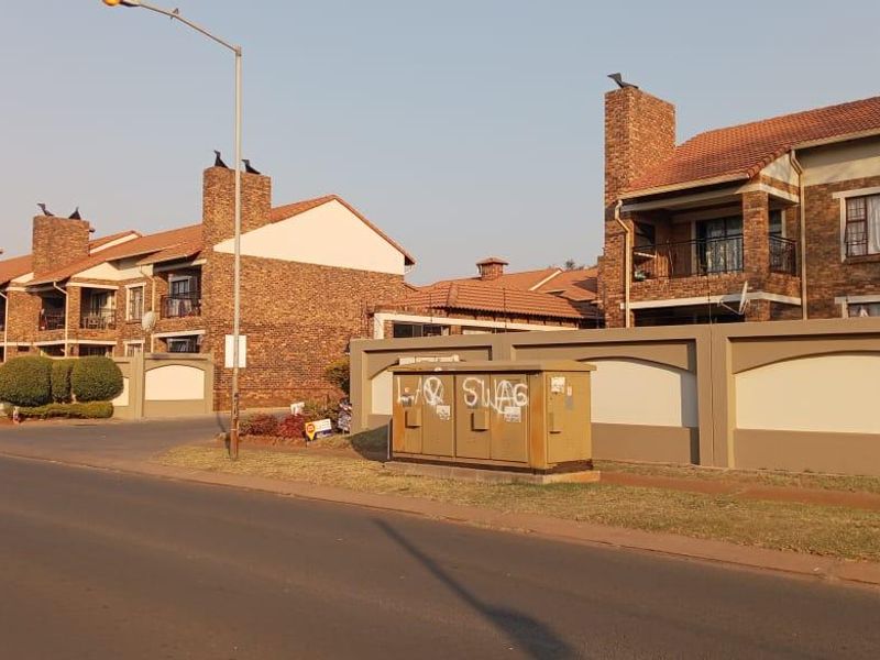 Street view of a multi-unit townhouse complex featuring face-brick construction, tiled roofs, and perimeter walling.