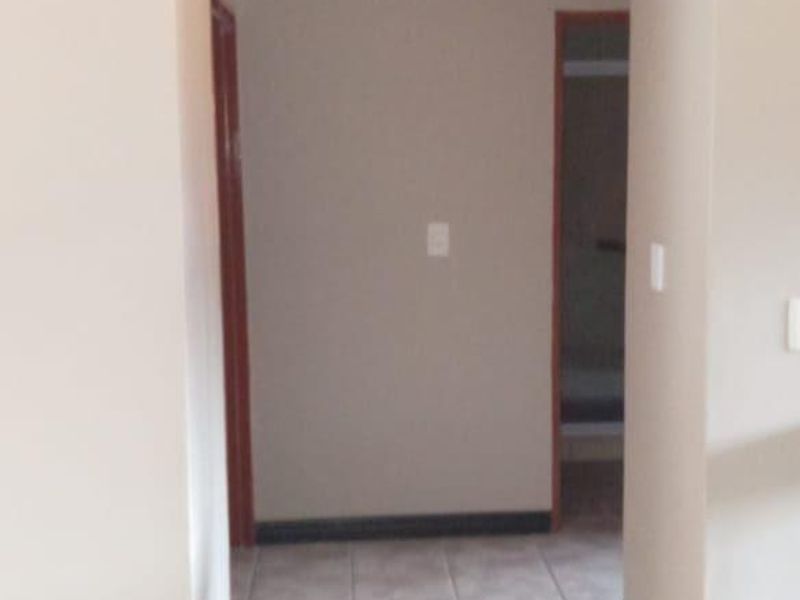 A clean, empty hallway featuring neutral wall tones, tiled flooring, and coving, providing access to adjacent rooms through internal doorways.