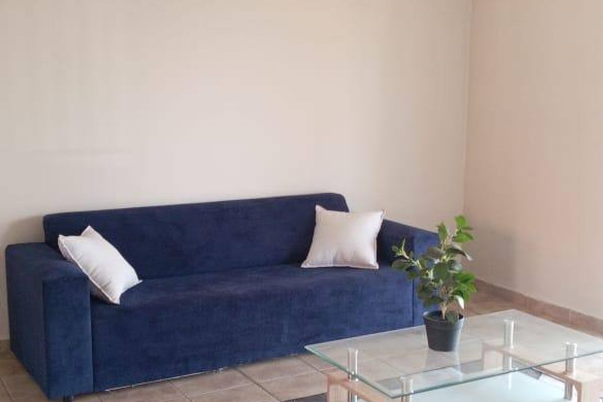 A simple living room area featuring neutral wall tones, tiled flooring, and a ceiling-mounted light fixture.