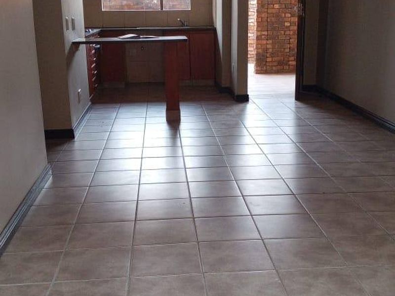 An open-plan living and kitchen area featuring neutral tiled flooring, built-in cabinetry, and a breakfast bar, leading to an exterior doorway.
