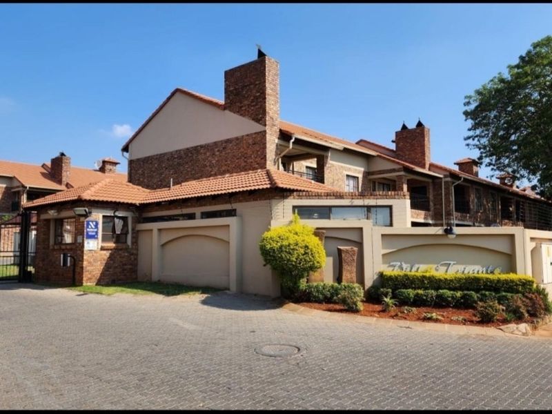 Front exterior view of the townhouse complex featuring brick facade, tiled roofing, secure gated entrance, and perimeter wall with electric fencing.