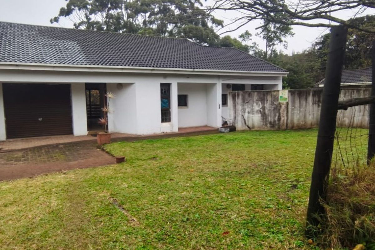 Rear view of the property featuring a tiled roof, single garage, and a large garden area with a concrete boundary wall.