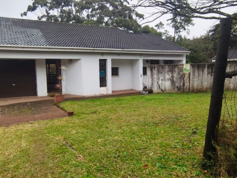 Rear view of the property featuring a tiled roof, single garage, and a large garden area with a concrete boundary wall.